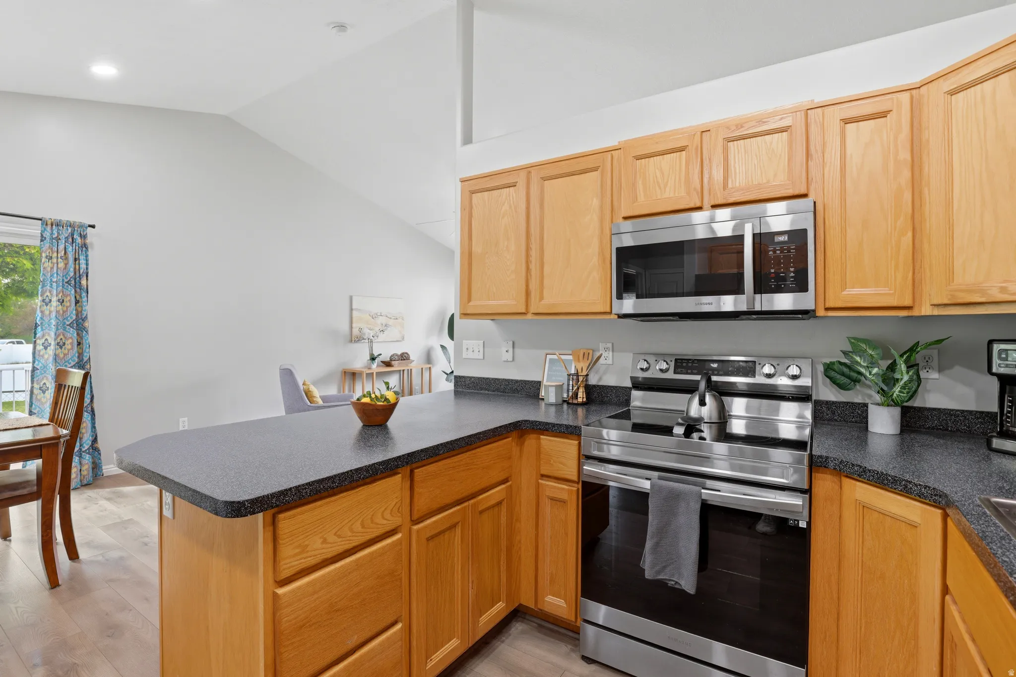 Kitchen with a peninsula, stainless steel appliances, dark countertops, lofted ceiling, and light wood-type flooring