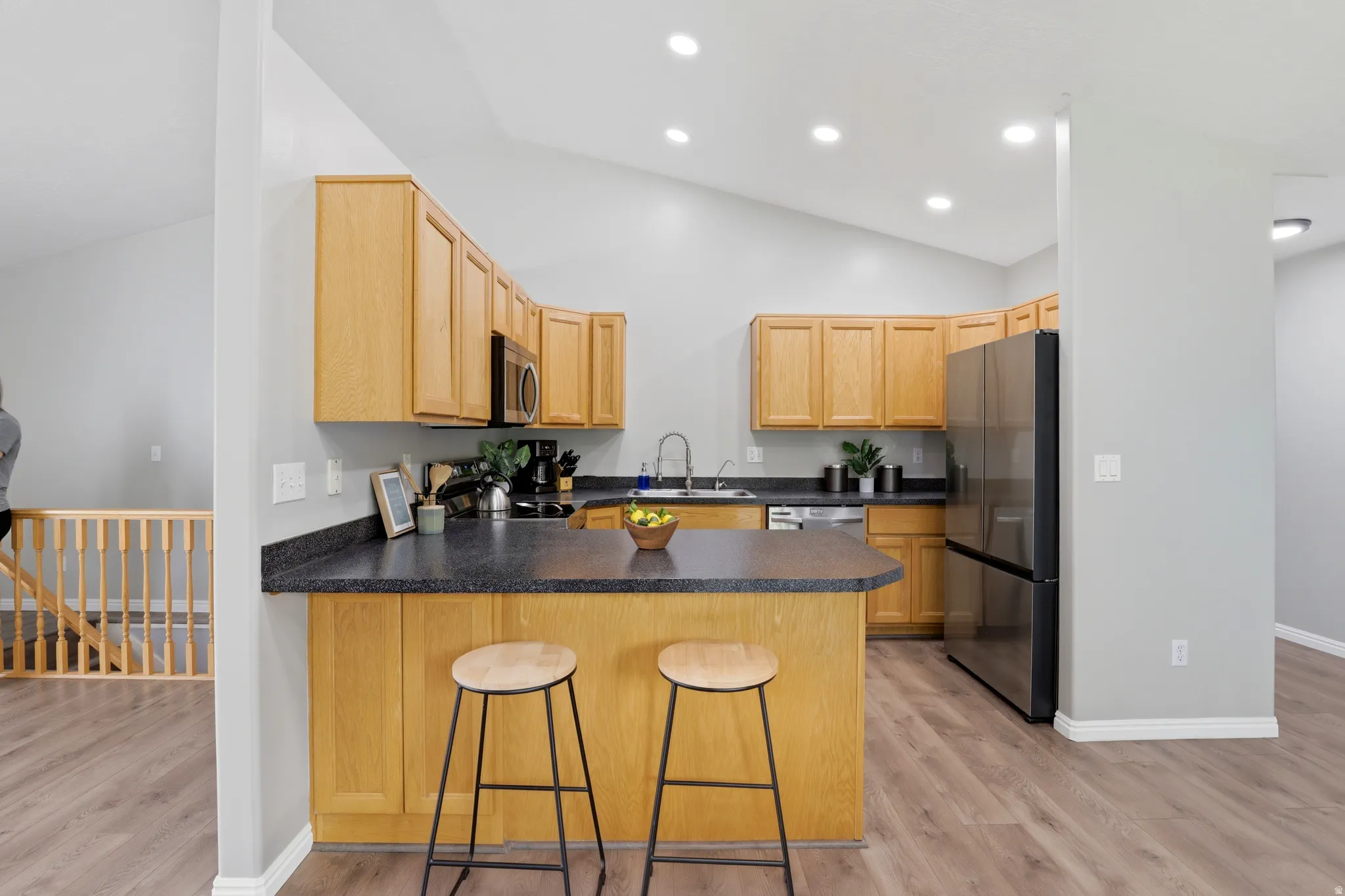 Kitchen featuring a peninsula, stainless steel appliances, light wood-type flooring, a kitchen bar, and lofted ceiling