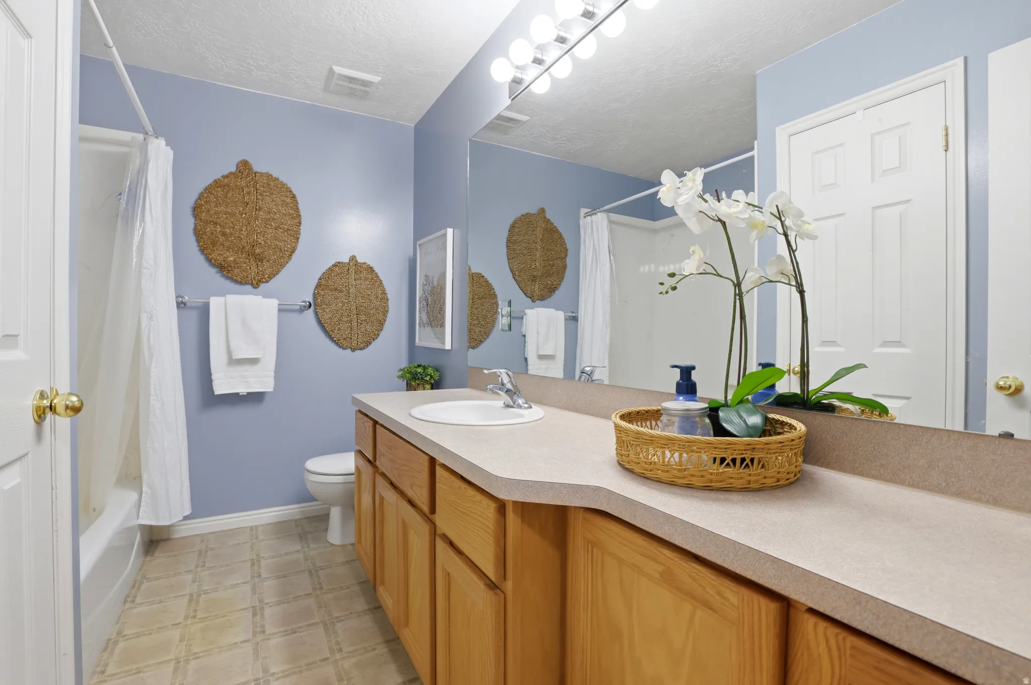 Bathroom with vanity, a textured ceiling, shower / bath combination with curtain, and light flooring