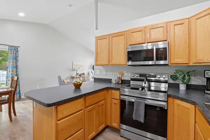 Kitchen with a peninsula, stainless steel appliances, dark countertops, lofted ceiling, and light wood-type flooring