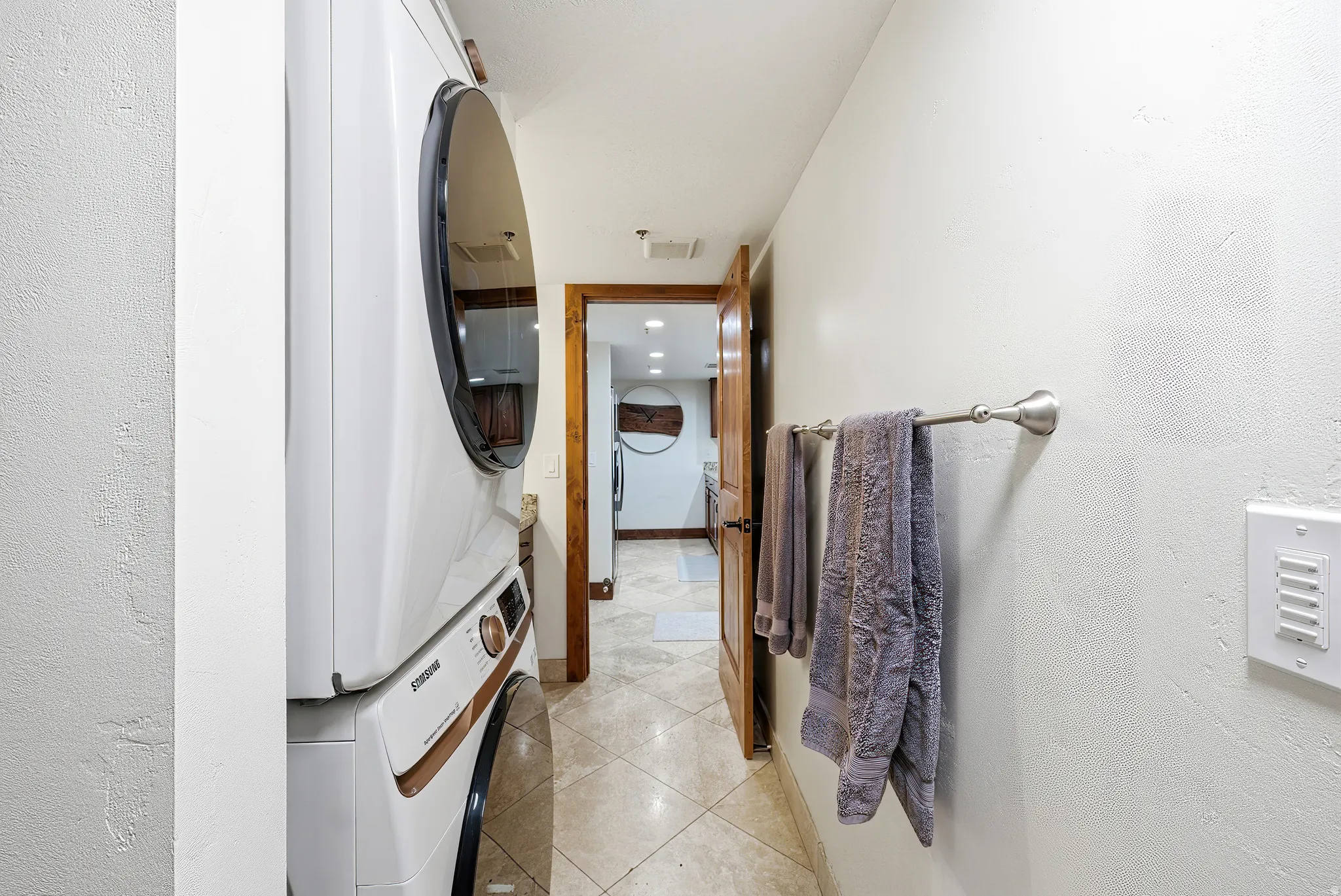 Laundry area with light tile patterned floors, stacked washing machine and dryer, recessed lighting, and a textured wall