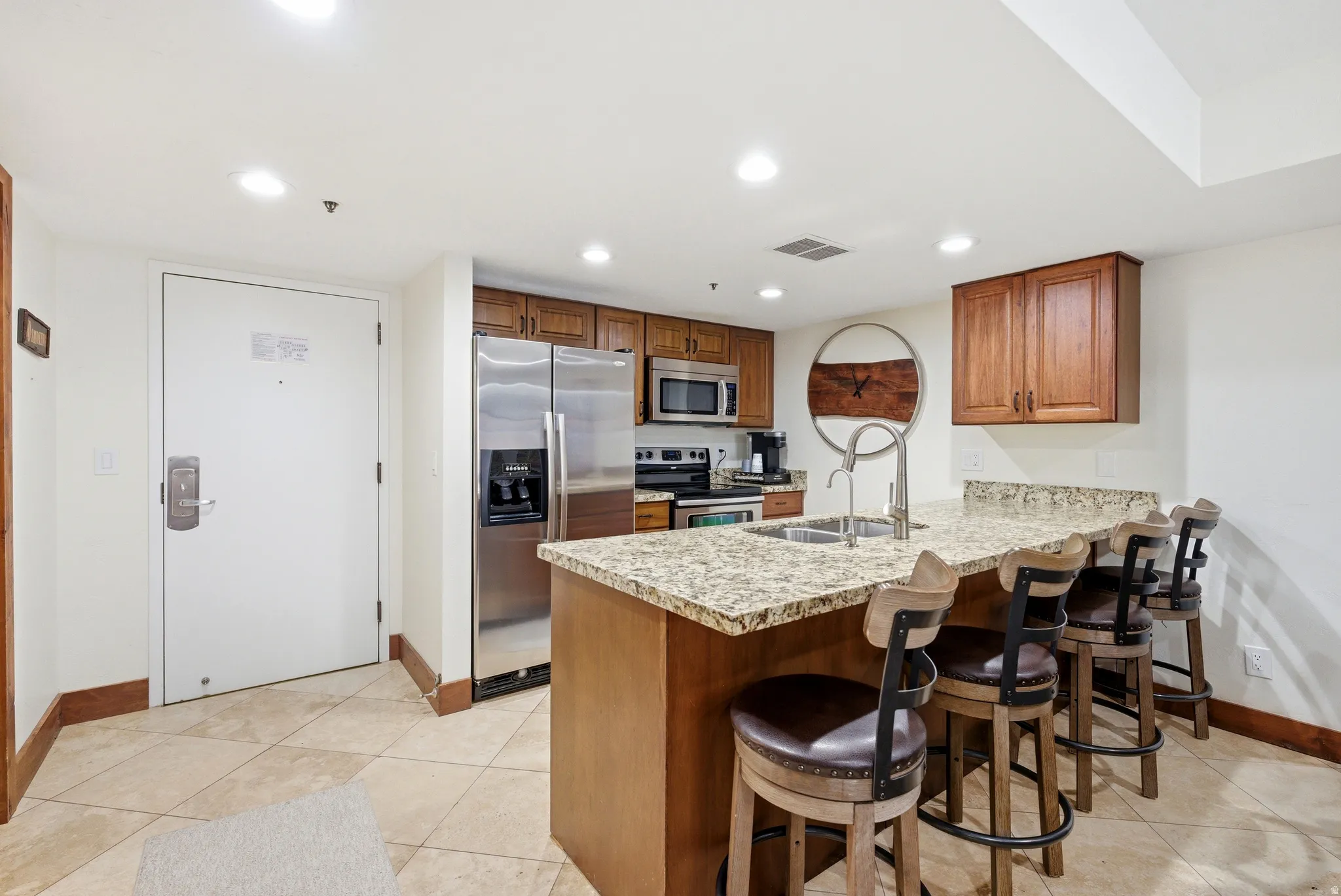 Kitchen with a kitchen bar, a peninsula, wood finish cabinetry, stainless steel appliances, and recessed lighting