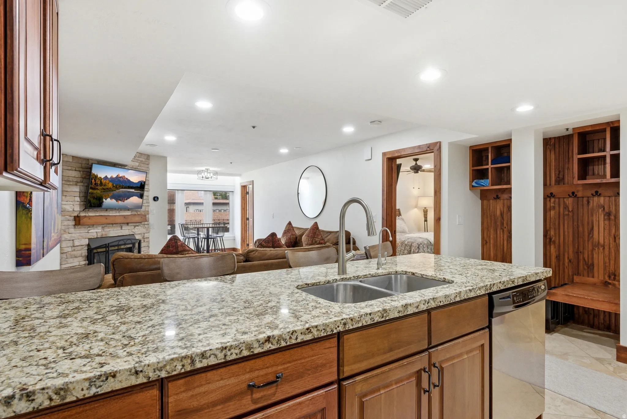 Kitchen featuring open floor plan, wood finish cabinetry, ceiling fan, light stone counters, and a stone fireplace