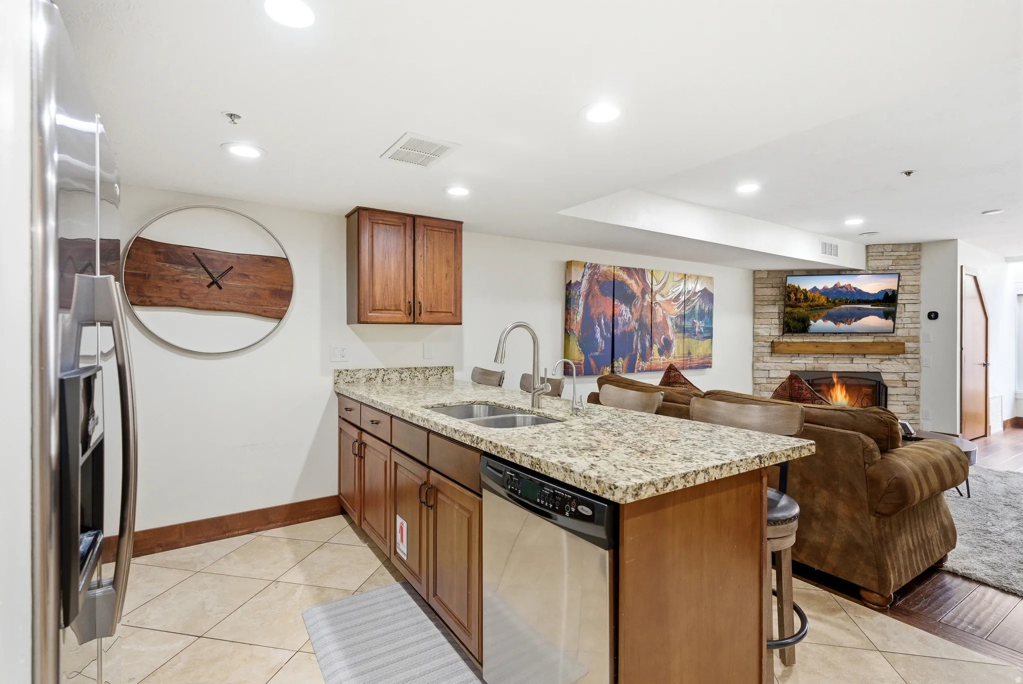 Kitchen with a peninsula, light stone counters, a fireplace, wood finish cabinets, and a kitchen breakfast bar