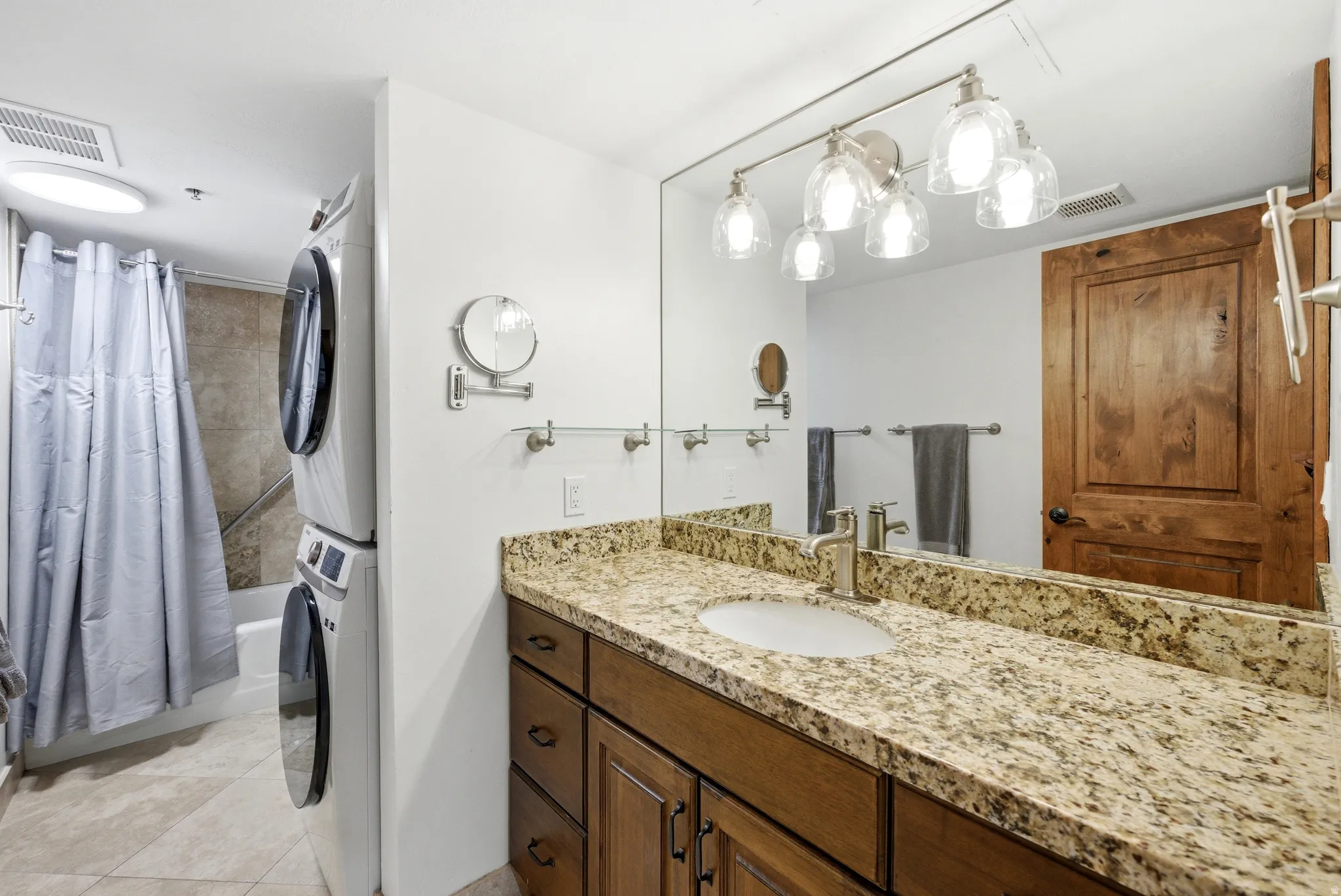 Bathroom with vanity, light tile patterned flooring, stacked washer and clothes dryer, and shower / tub combo