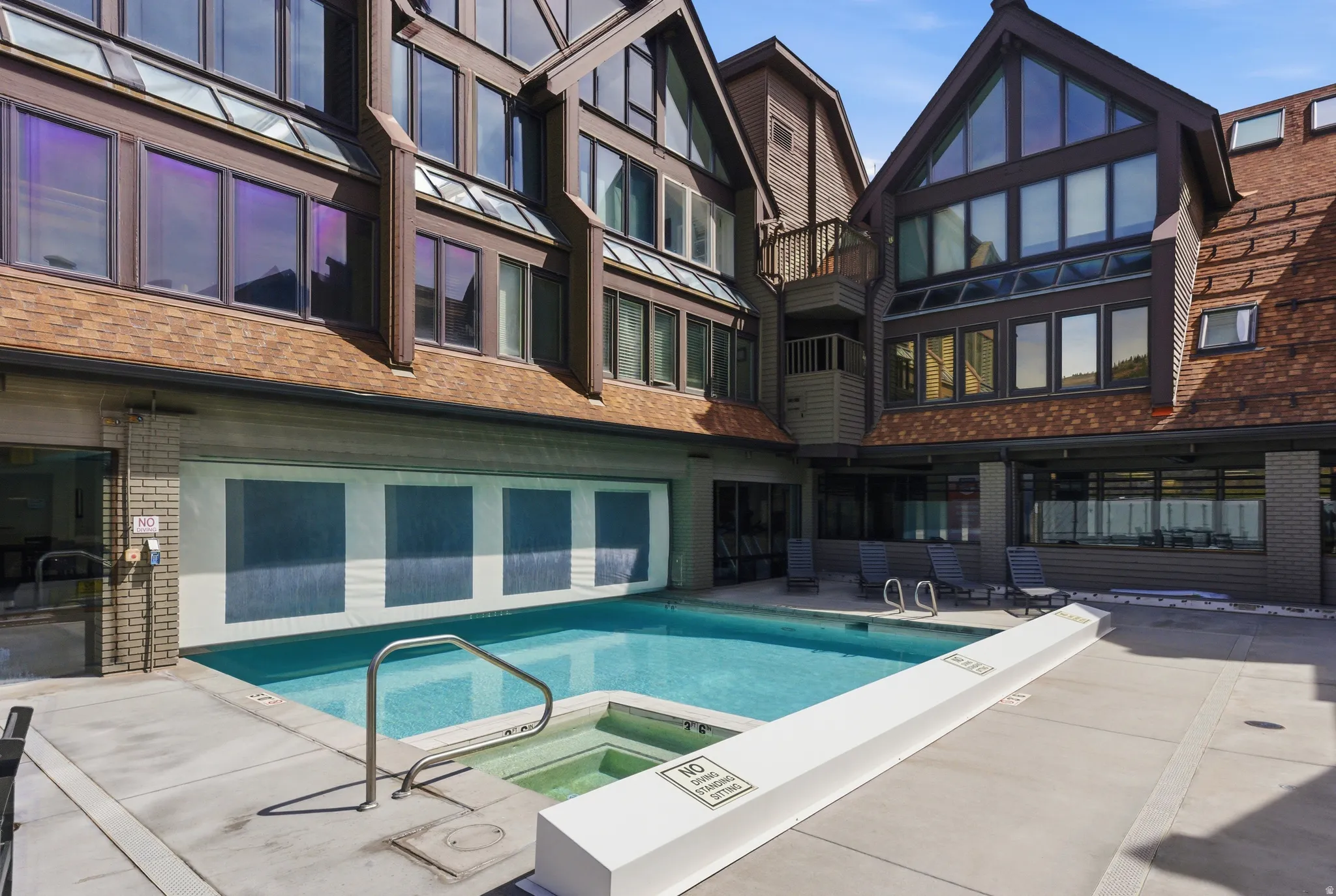 Back of property featuring brick siding, a pool with connected hot tub, a balcony, and a patio area