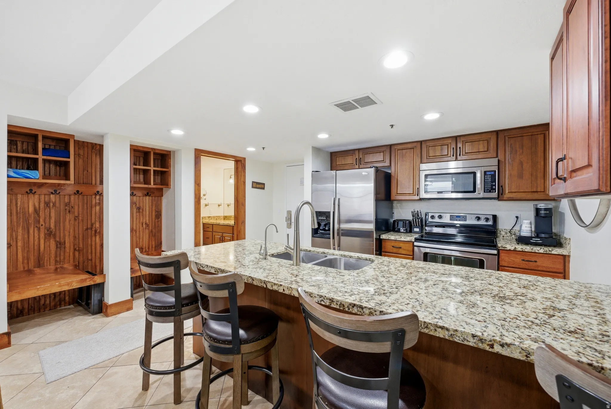 Kitchen featuring wood finish cabinets, light stone counters, a breakfast bar area, stainless steel appliances, and recessed lighting