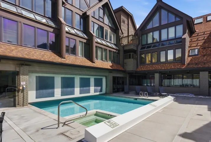Back of property featuring brick siding, a pool with connected hot tub, a balcony, and a patio area