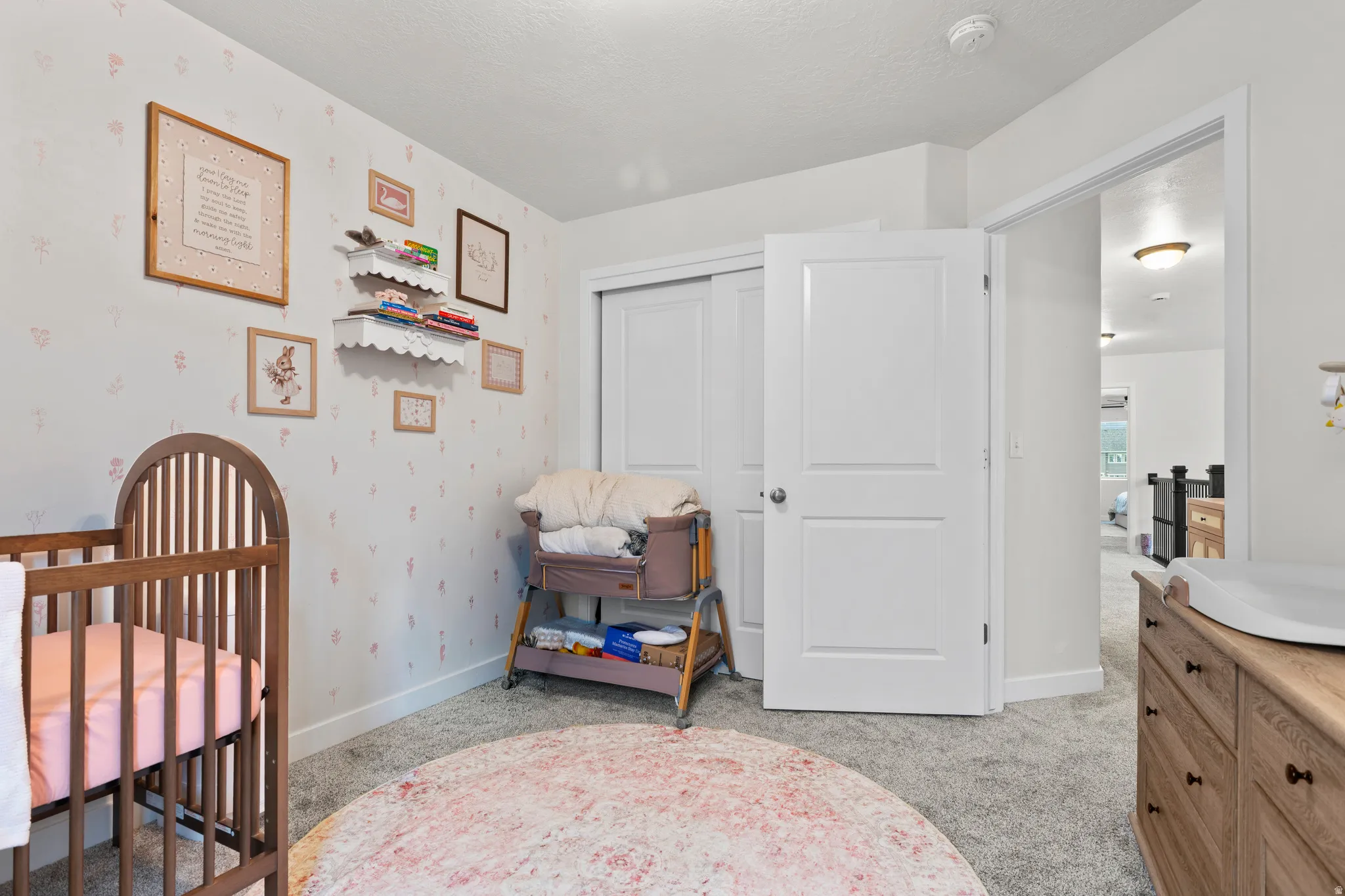 Bedroom featuring light carpet, a nursery area, and a closet