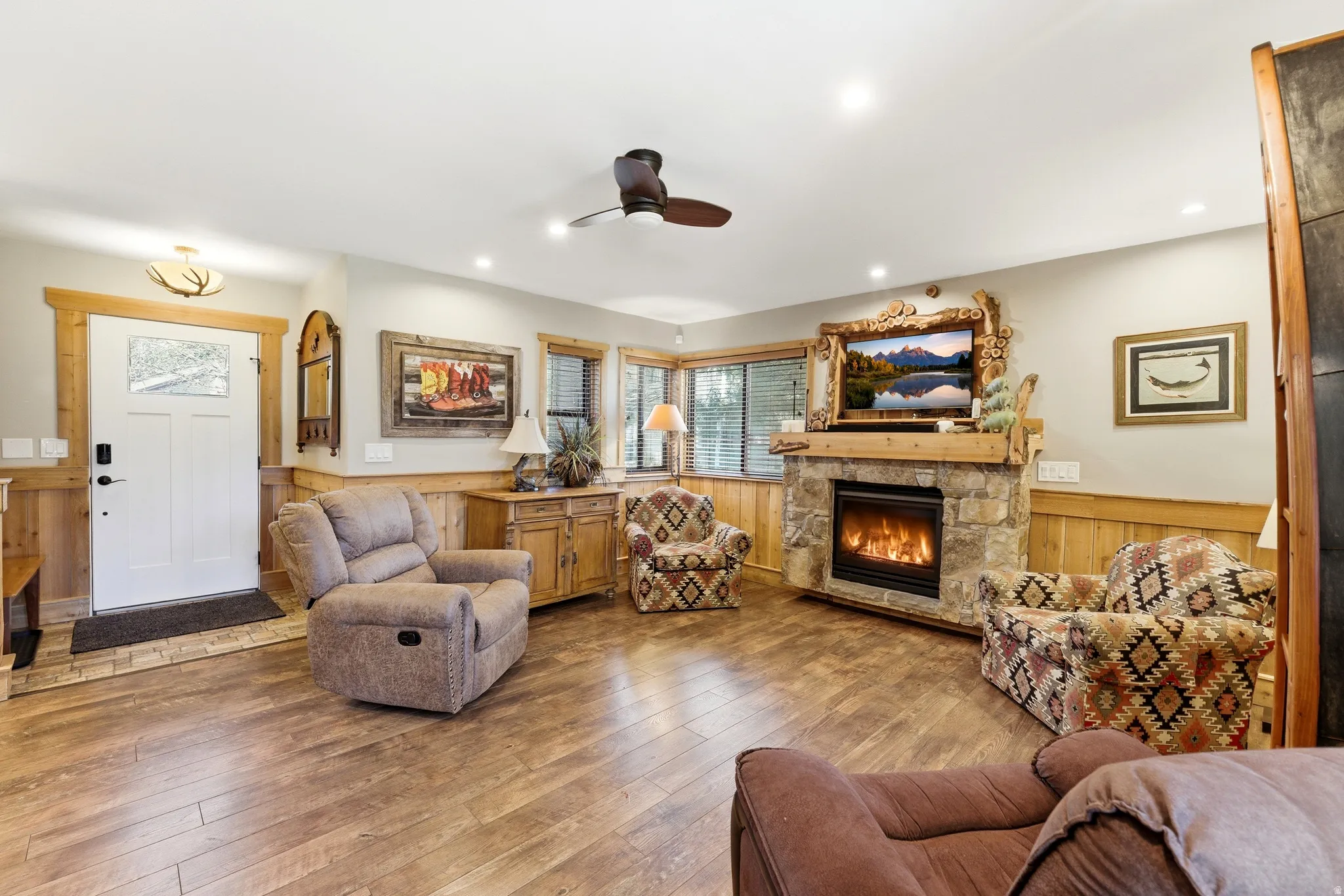 Living room with wainscoting, ceiling fan, a fireplace, wood walls, and wood-type flooring