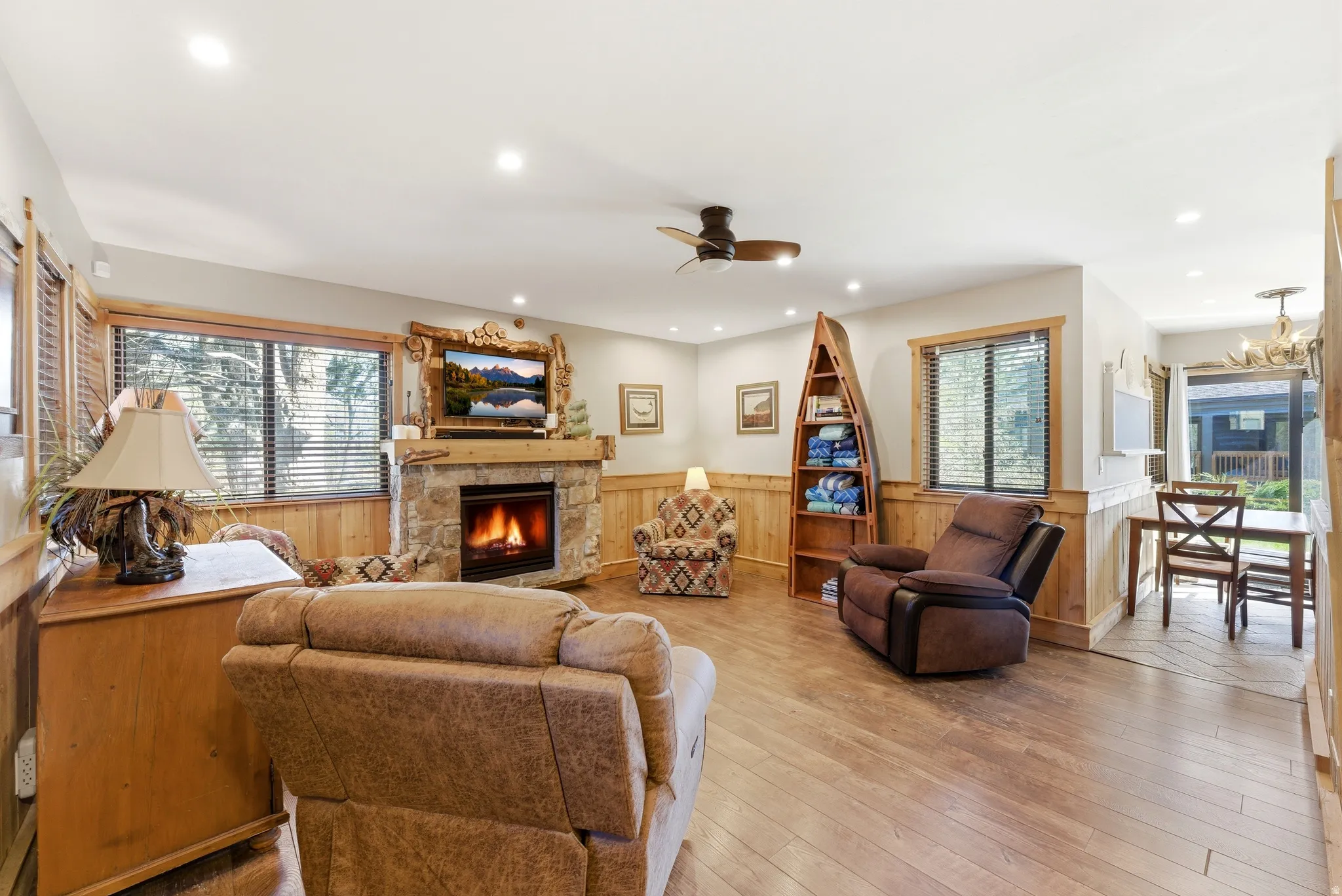 Living area featuring a wainscoted wall, a stone fireplace, a ceiling fan, wood walls, and light wood finished floors