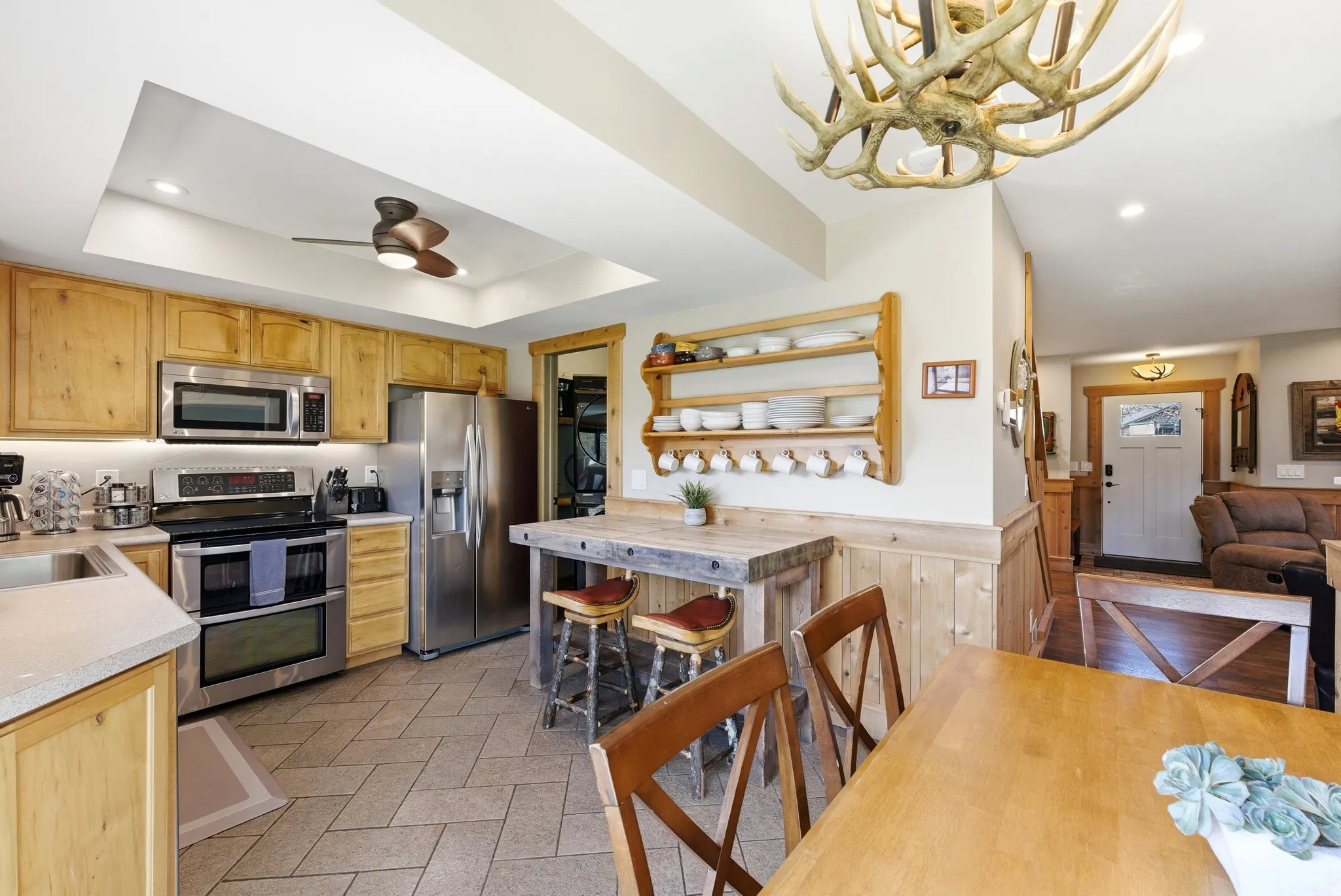 Kitchen featuring light wood finish cabinetry, light countertops, stainless steel appliances, a wainscoted wall, and decorative light fixtures