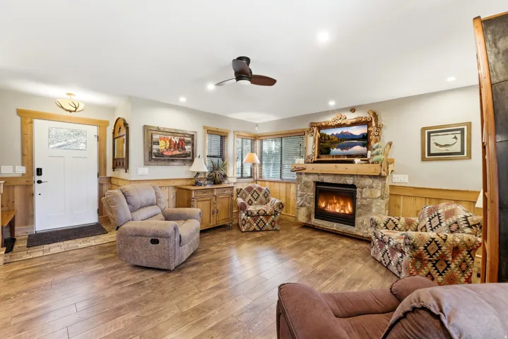 Living room with wainscoting, ceiling fan, a fireplace, wood walls, and wood-type flooring