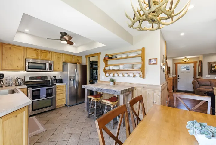 Kitchen featuring light wood finish cabinetry, light countertops, stainless steel appliances, a wainscoted wall, and decorative light fixtures