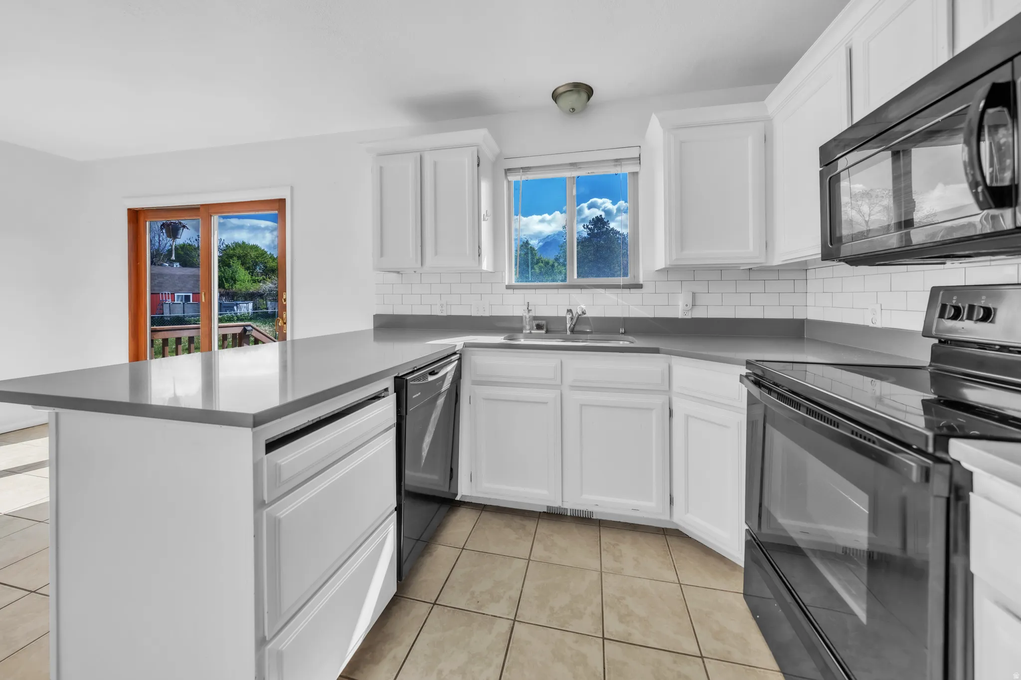 Kitchen with black appliances, white cabinets, a peninsula, light tile patterned floors, and backsplash