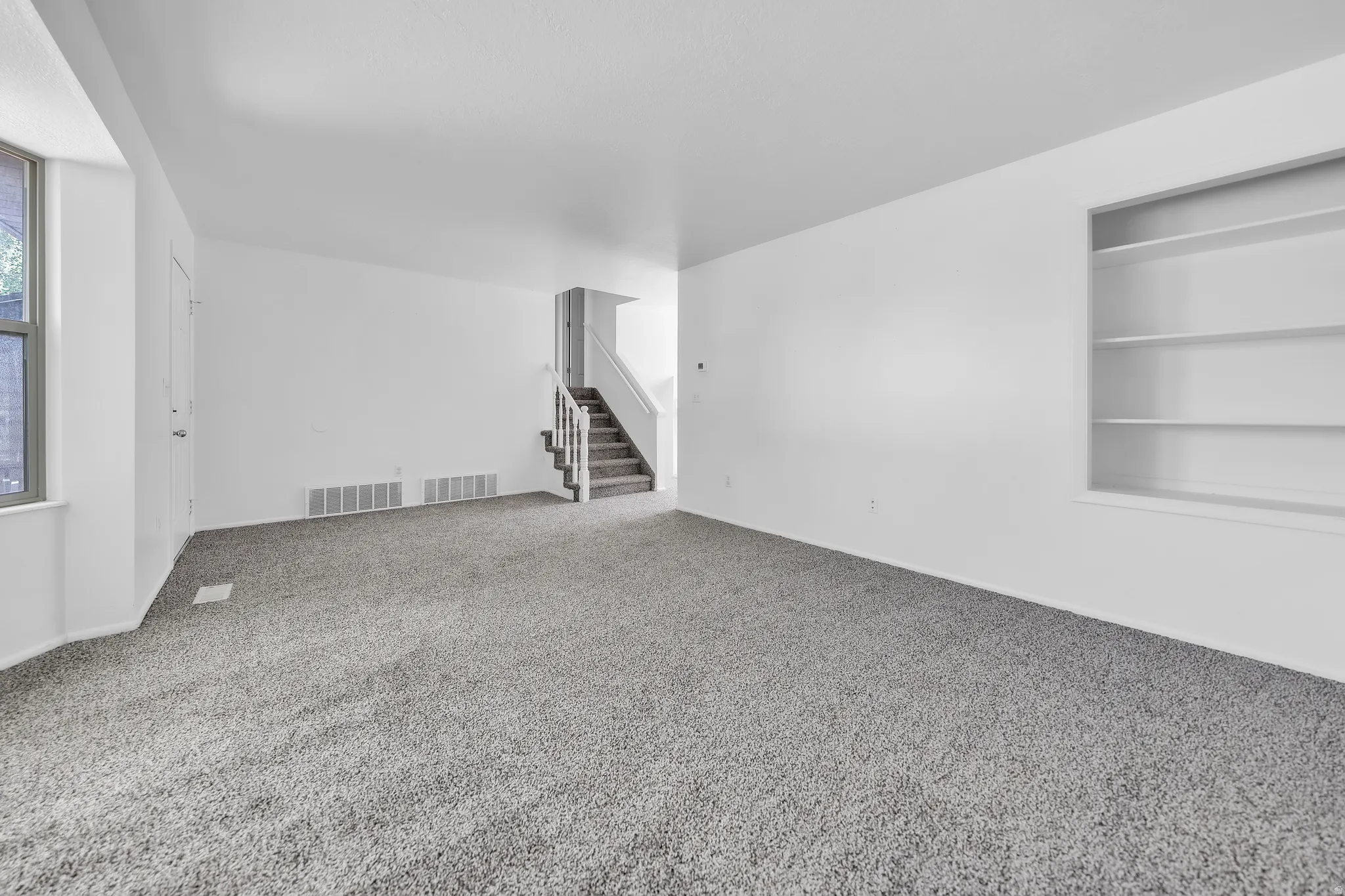 Spacious interior room featuring light grey carpet, white walls, and a prominent built-in shelving unit