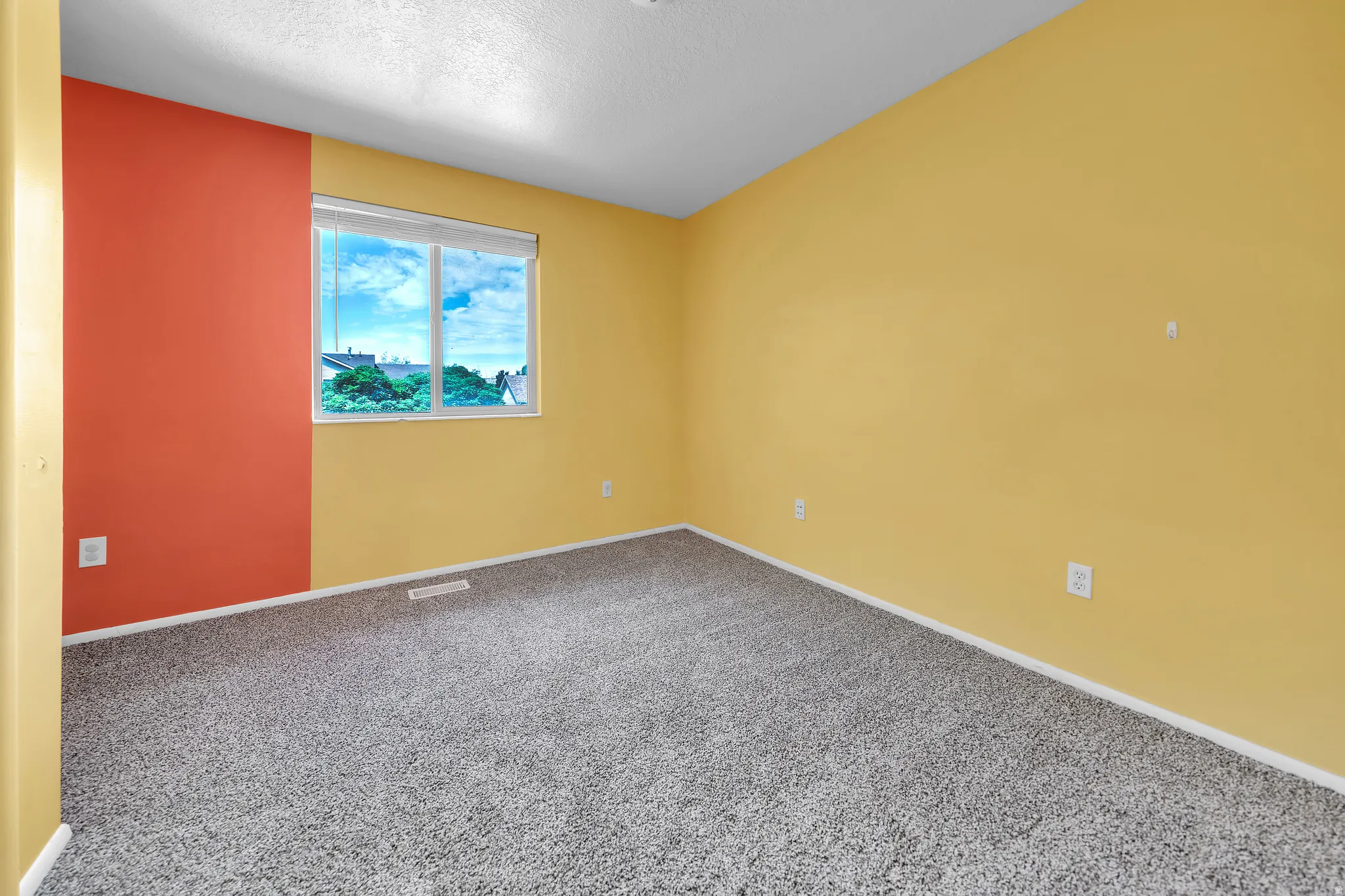 Room featuring light gray carpeting, a large window with white blinds, and walls painted in yellow and a contrasting red accent