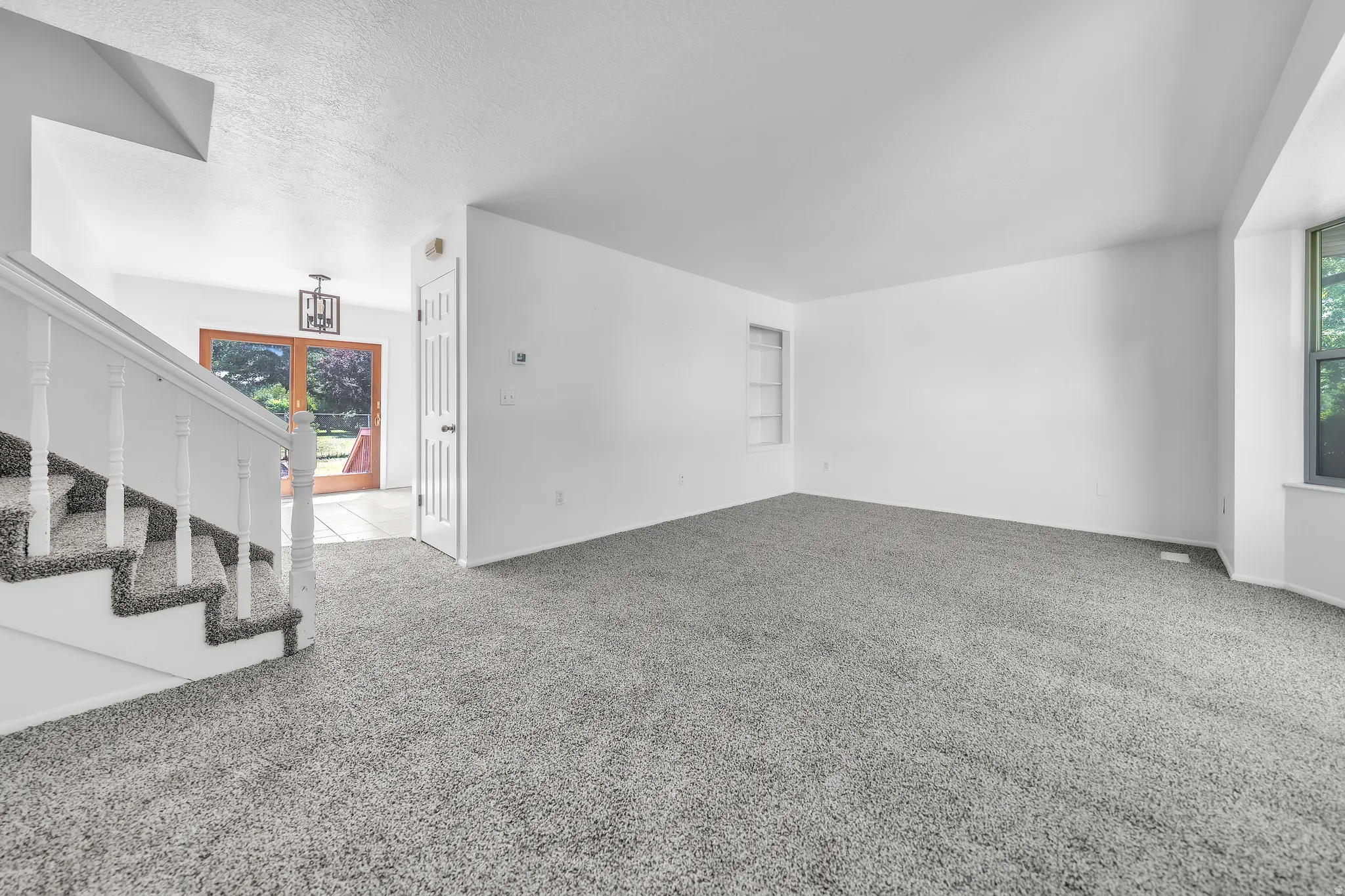 Spacious living area featuring grey carpeting, white walls, and a built-in shelving unit