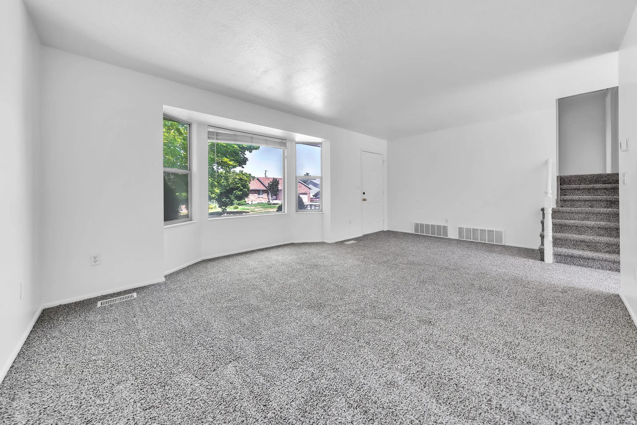 Expansive living space featuring light gray carpet, white walls, and a bay window with multiple panes