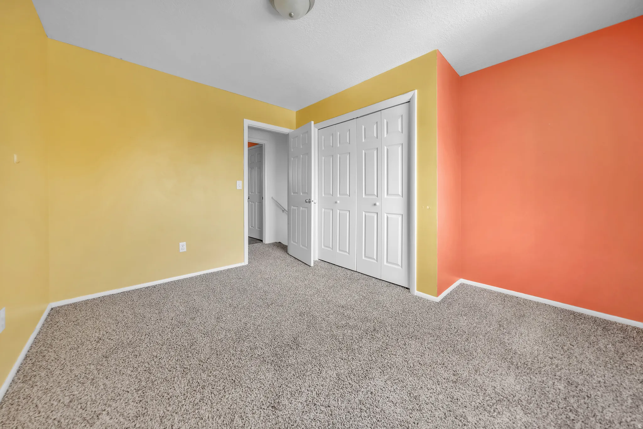 Carpeted interior space featuring bright yellow and orange walls, white trim, and a white bi-fold closet