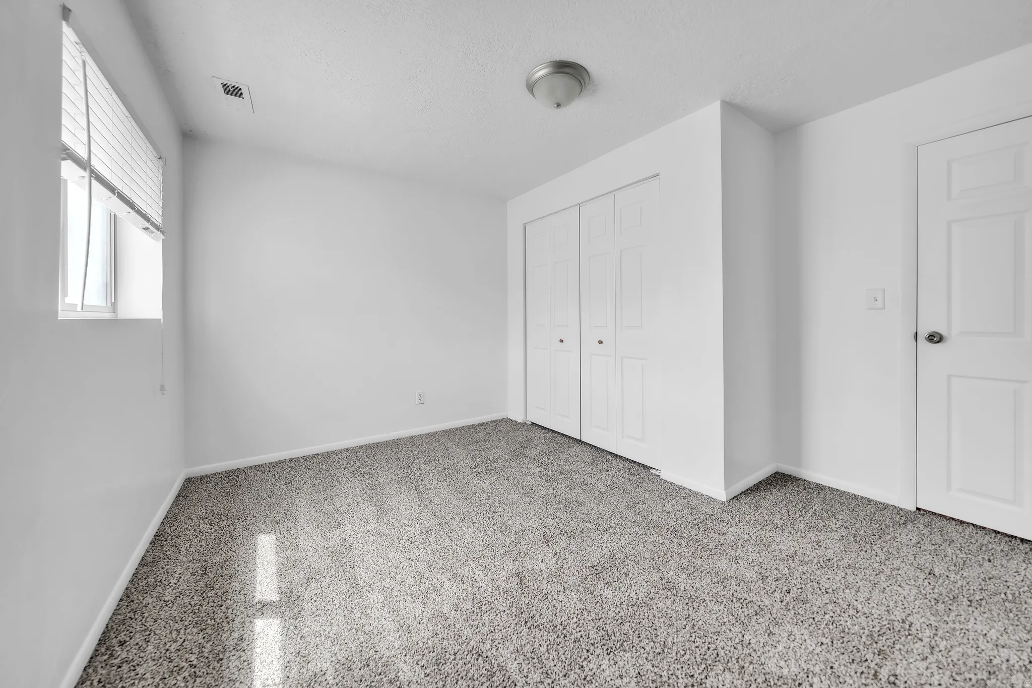 Spacious room featuring neutral carpeting, white walls, and a window with blinds