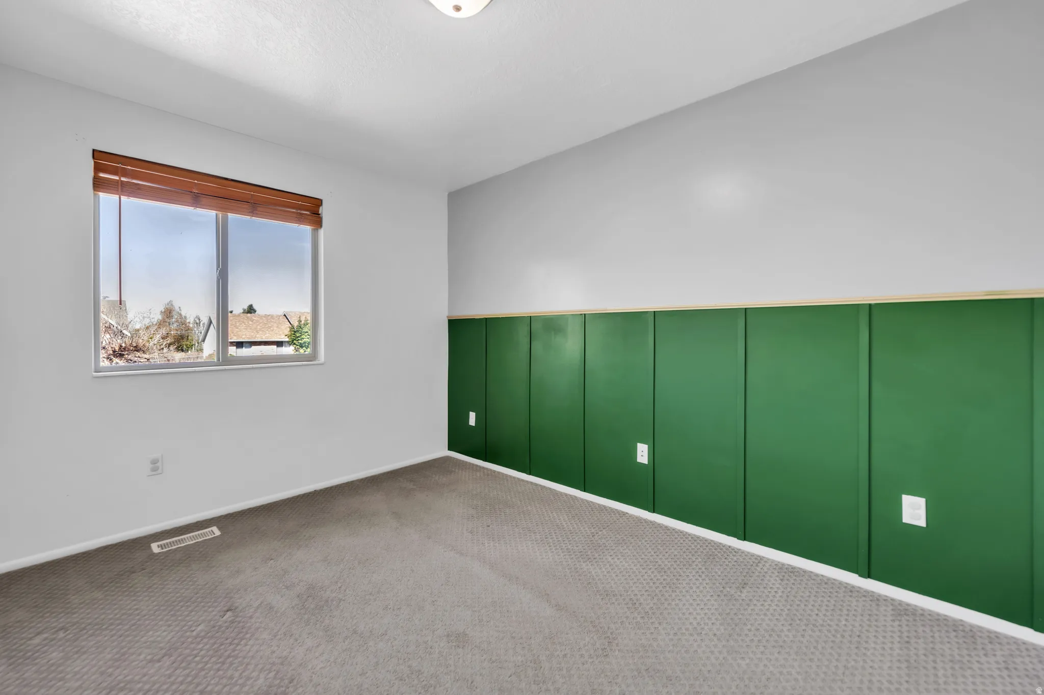 Unfurnished room featuring carpet, a decorative wall, and wainscoting