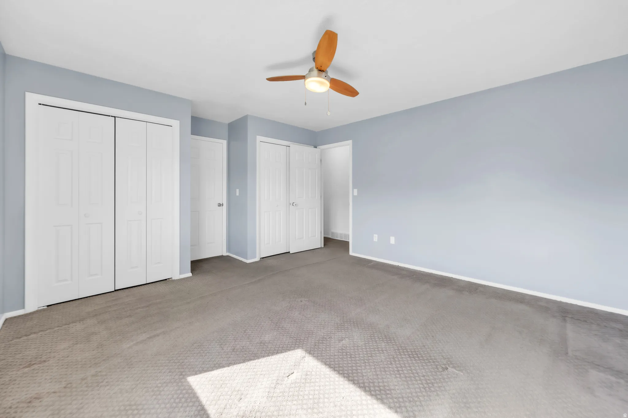 Unfurnished bedroom featuring two closets, carpet, and ceiling fan