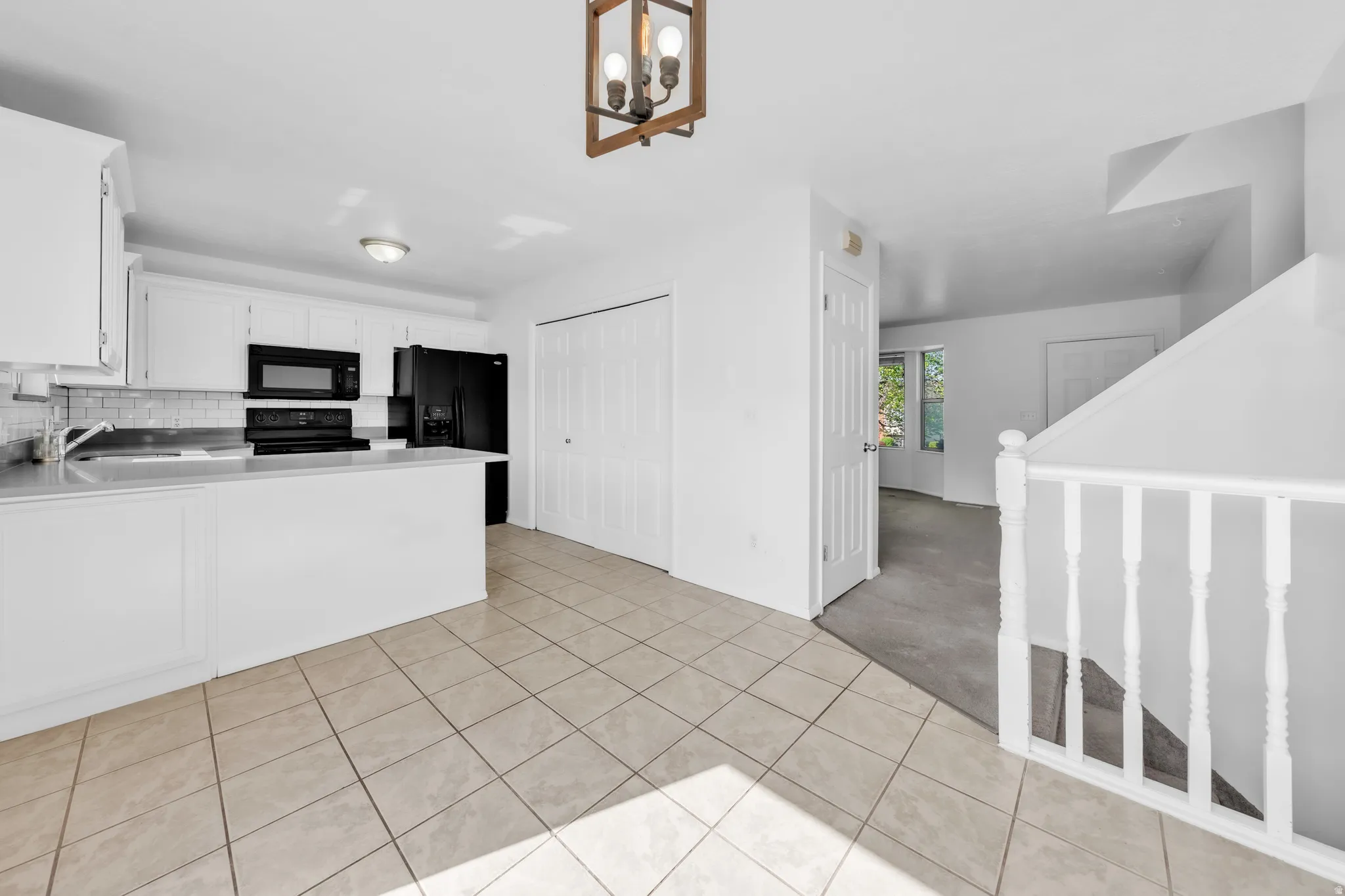Kitchen featuring light countertops, white cabinetry, a peninsula, black appliances, and light tile patterned floors
