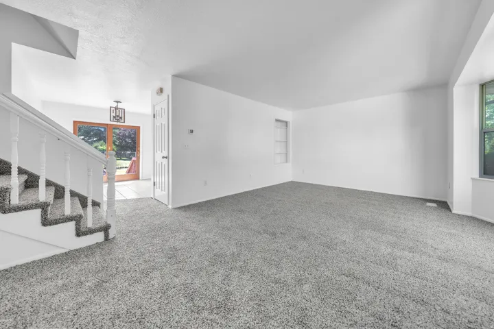 Spacious living area featuring grey carpeting, white walls, and a built-in shelving unit