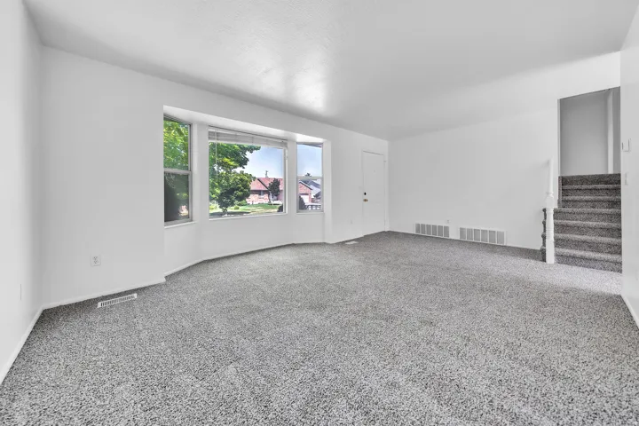 Expansive living space featuring light gray carpet, white walls, and a bay window with multiple panes