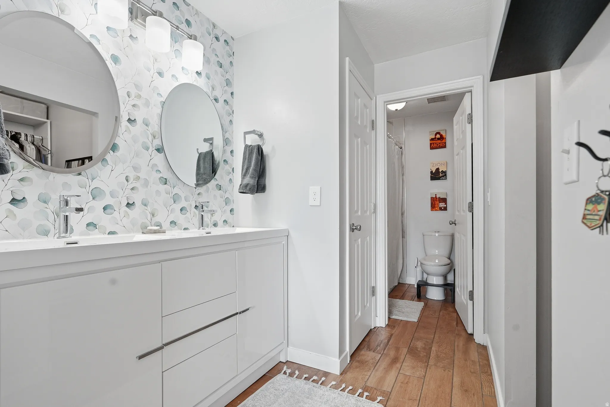 Full bath featuring double vanity, light wood-style floors, and curtained shower