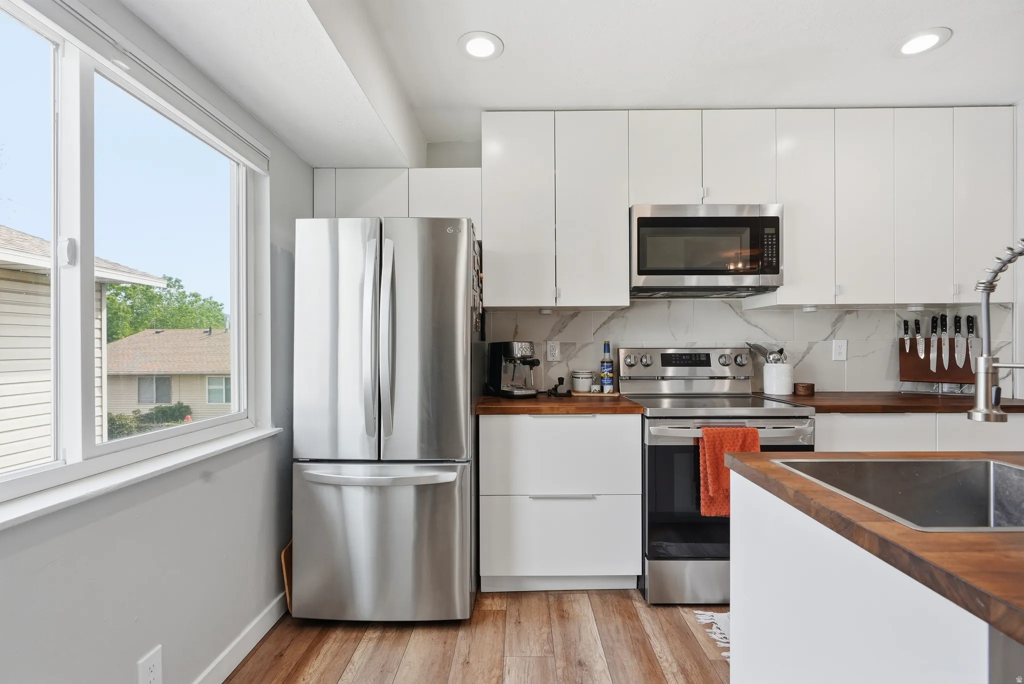 Kitchen featuring stainless steel appliances, wooden counters, white cabinetry, light wood finished floors, and recessed lighting