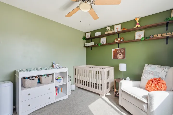 Carpeted bedroom with a nursery area and ceiling fan