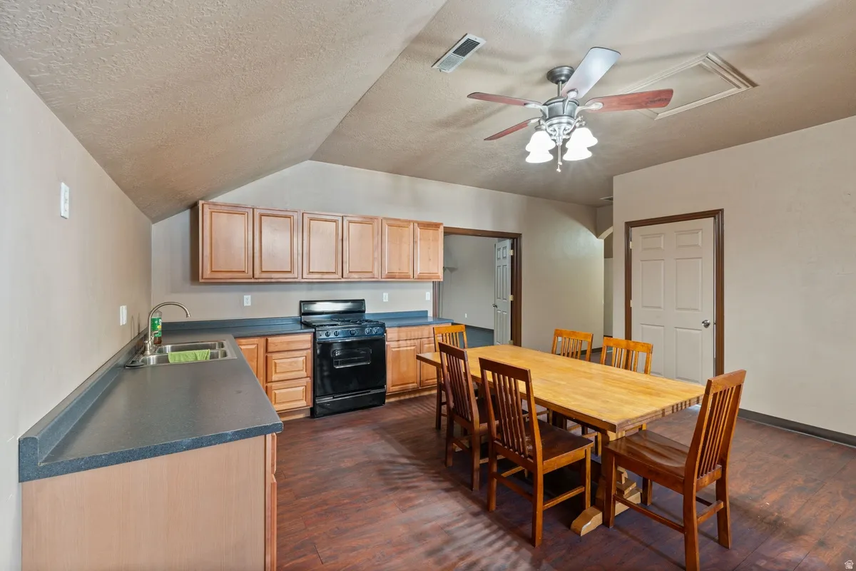 Kitchen featuring dark countertops, black gas range, ceiling fan, and dark wood-style floors