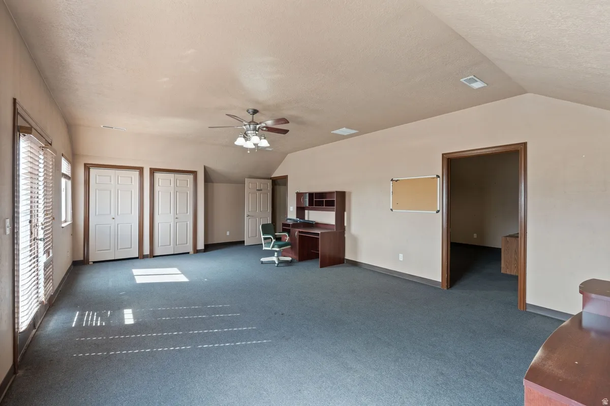Unfurnished living room featuring a ceiling fan, a textured ceiling, dark colored carpet, and a desk