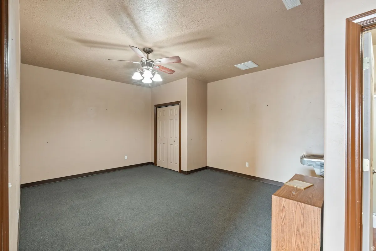 Empty room featuring dark colored carpet, a textured ceiling, and a ceiling fan