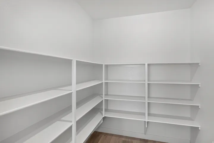 Corner pantry featuring white shelving, multiple storage levels, and wood-finish flooring