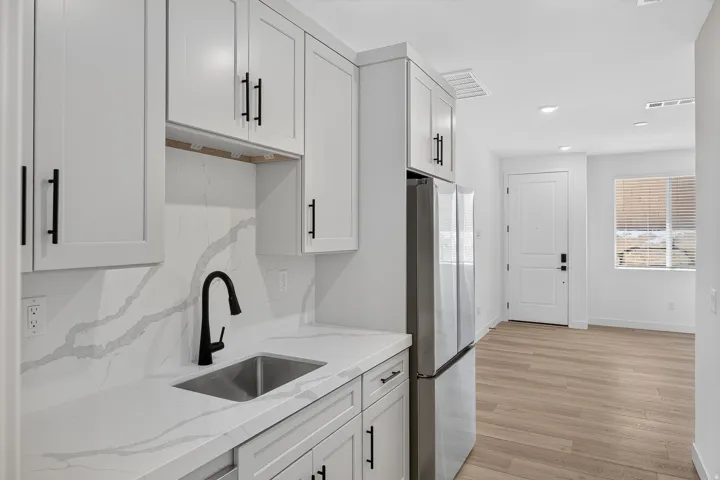 Modern kitchen featuring white shaker-style cabinetry with black hardware, marble-look quartz countertops, stainless steel appliances including a refrigerator and range hood, an undermount sink with matte black faucet, and white subway tile backsplash