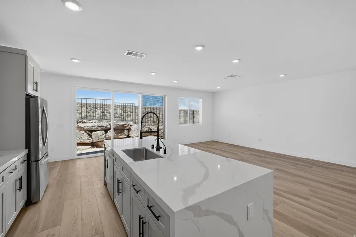 Modern kitchen featuring a large waterfall-edge island with white quartz countertop, stainless steel appliances including a side-by-side refrigerator, undermount sink with contemporary faucet, white cabinetry with hardware accents, recessed ceiling lighti