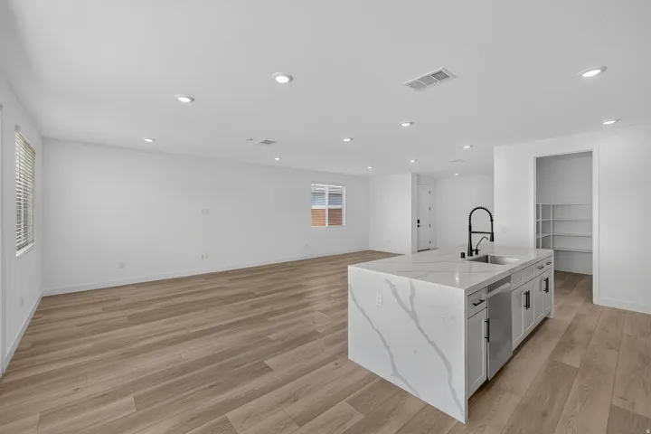 Spacious open-concept interior featuring light wood-finish flooring, recessed lighting, and a kitchen island with a waterfall countertop