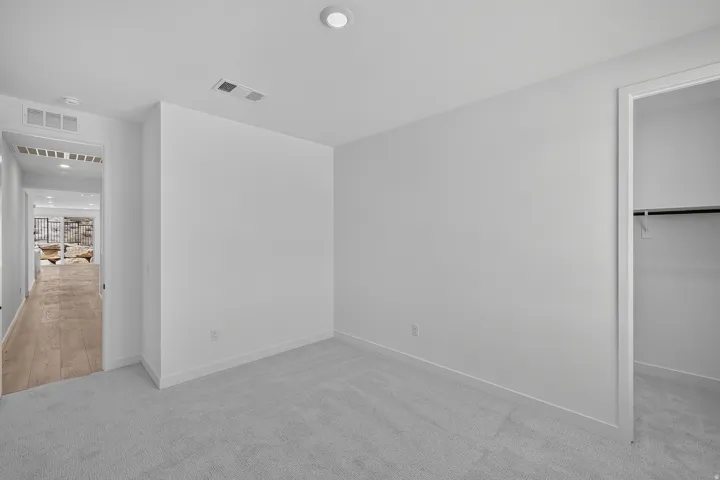 Spacious bedroom featuring fresh white walls, recessed ceiling lighting, and direct access to a walk-in closet with shelving