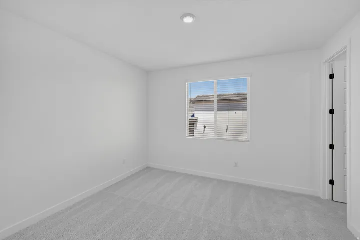 Bright interior space featuring a window with blinds, recessed lighting, light gray carpet, white walls, and a white door with black hardware