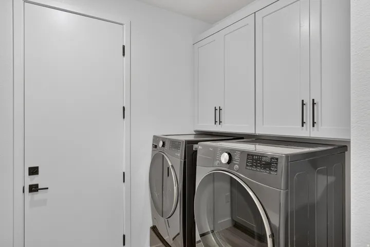 Modern laundry area featuring light gray cabinetry with matte black hardware, a light gray flat-panel door with matte black hardware, and textured white walls