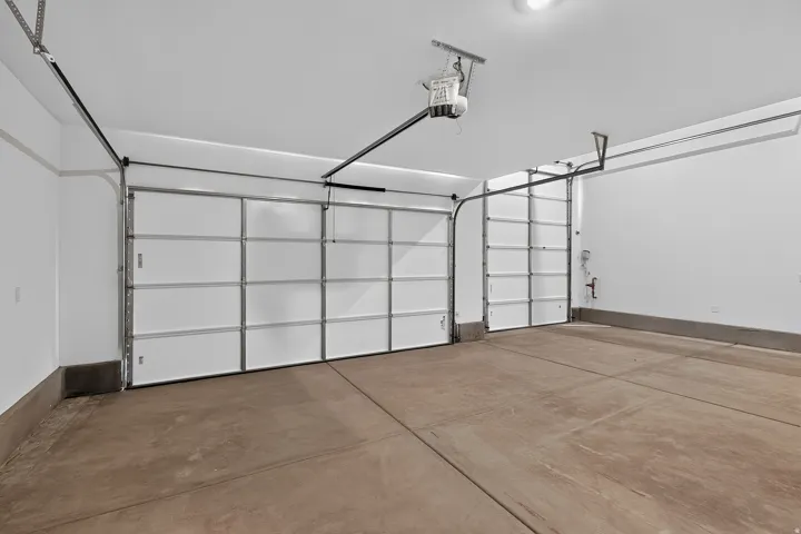 Spacious garage featuring two overhead doors, concrete flooring, overhead lighting, and white painted walls