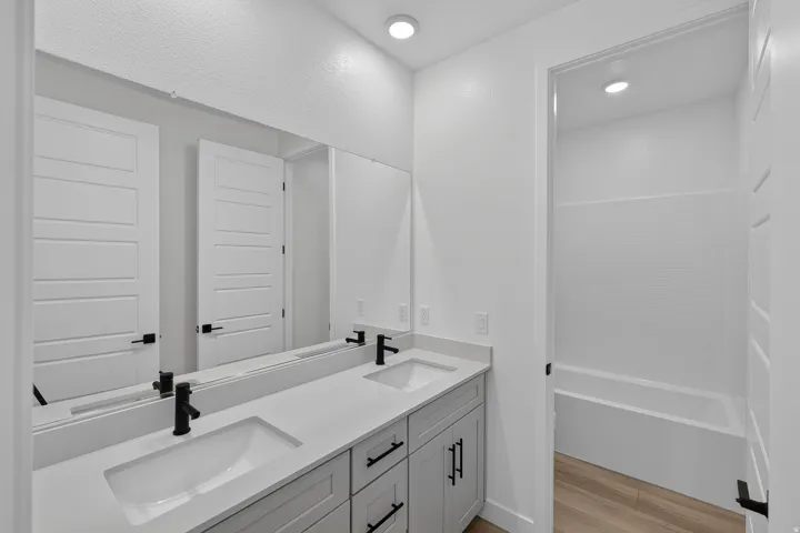 Modern bathroom featuring a dual vanity with light gray cabinetry, white countertops, and matte black fixtures