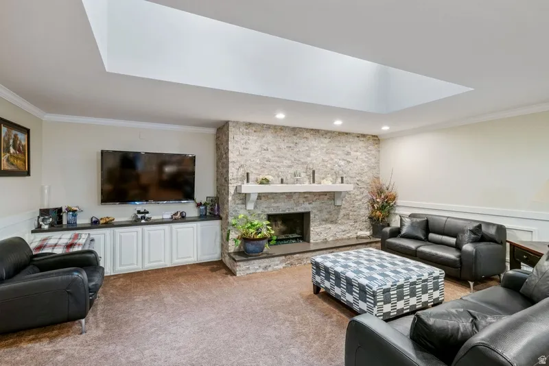 Living room with crown molding, carpet, a fireplace, recessed lighting, and a wainscoted wall