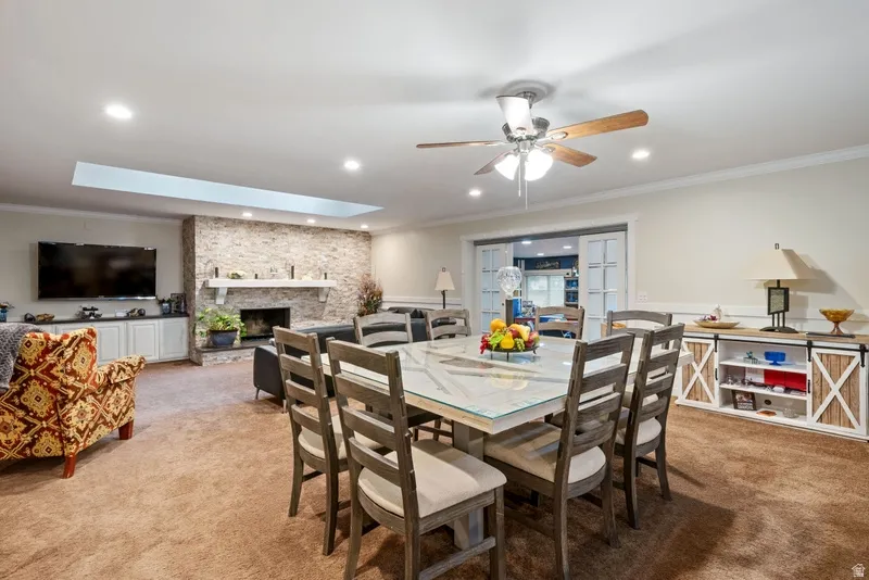 Dining room with crown molding, a stone fireplace, a skylight, carpet floors, and a ceiling fan