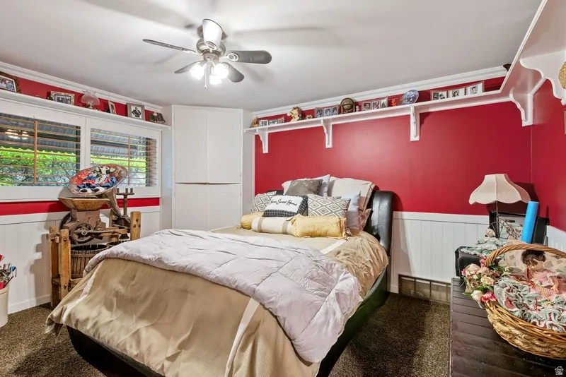 Bedroom featuring a wainscoted wall, ceiling fan, crown molding, and dark carpet