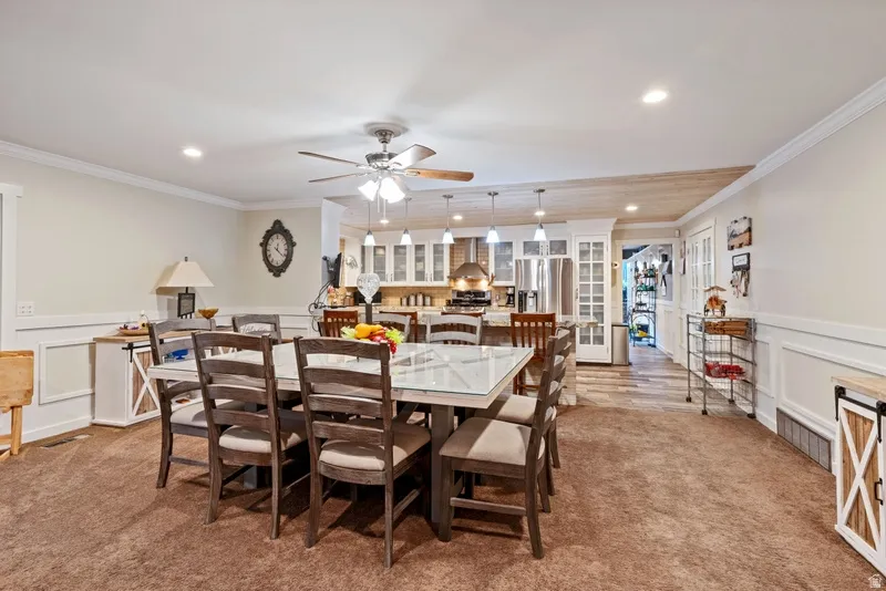 Dining room featuring a decorative wall, wainscoting, light carpet, a ceiling fan, and crown molding