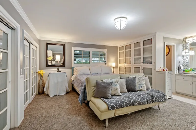 Bedroom with light colored carpet, crown molding, and ensuite bath